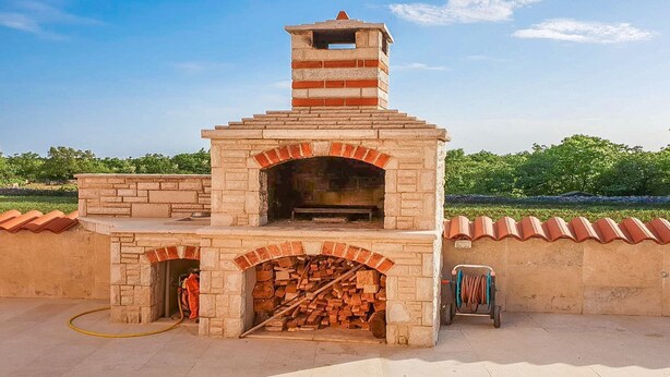 Un horno de ladrillo al aire libre con una chimenea, un espacio para almacenar leña y una manguera.