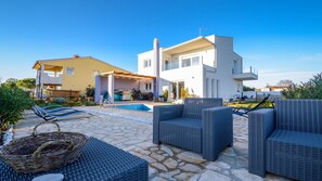 Una casa moderna con piscina, mobiliario de exterior y un patio cubierto.