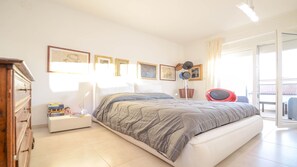 Un dormitorio con una cama, mesitas de noche, un aparador y una ventana con cortinas.