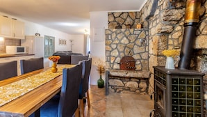A cozy living room with a stone fireplace, a dining area with a wooden table, and a kitchen with white cabinets and a microwave.