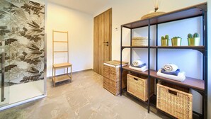 A hallway with a wooden door, a wooden chair, wicker baskets, and shelves with towels and cacti.
