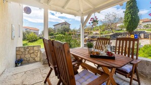 A covered outdoor seating area with a wooden table and chairs, a potted plant, and a view of the surrounding landscape.