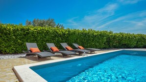 A swimming pool with lounge chairs and a hedge in the background.