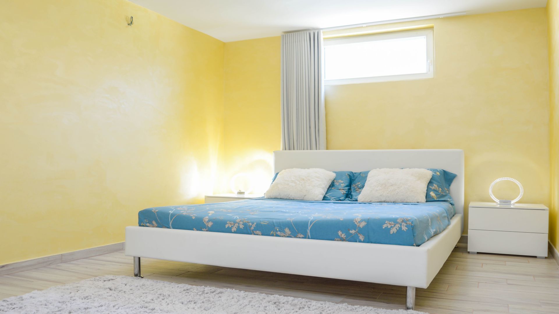 Un dormitorio con cama, mesita de noche y ventana con cortinas.