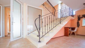 A staircase with a metal railing leading to a landing, a door on the left, and a small table with a chair in the foreground.