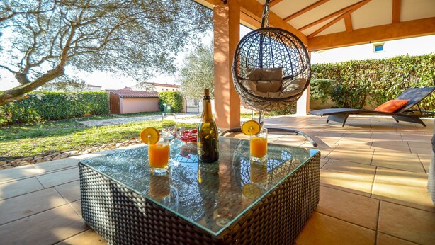 An outdoor patio with a glass-top table, wicker furniture, a hanging chair, and a view of the garden.