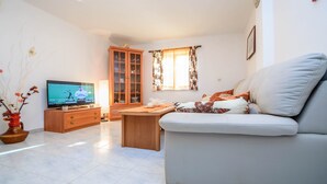 A living room with a sofa, a wooden cabinet, a television, and a window with curtains. - Holiday House Roses (Medulin)