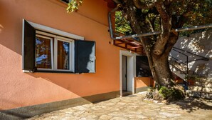 A building with a stone-paved entrance, a window with a closed shutter, and a tree in the foreground. - Holiday House Roses (Medulin)