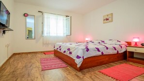 A bedroom with a wooden bed, a mirror, a window with curtains, a bedside lamp, and a small table. - Holiday House Roses (Medulin)