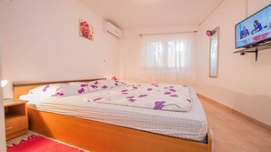 A bedroom with a bed, a TV, a window with curtains, and a small bedside table. - Holiday House Roses (Medulin)