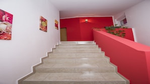 Una escalera con baldosas color crema y paredes rojas, que conduce a una habitación con una puerta y una lámpara fijada a la pared.
