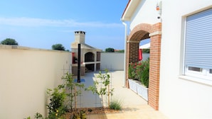 Una propiedad residencial con chimenea de ladrillo, un espacio cubierto al aire libre y un jardín con plantas en macetas.