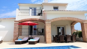 Ein zweistöckiges Haus mit Swimmingpool, Außenbereich mit Sitzgelegenheiten und einer überdachten Terrasse.