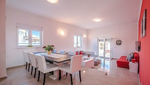 Una sala de estar moderna con comedor, con una mesa grande, sillas blancas, un sofá rojo y un dardo.