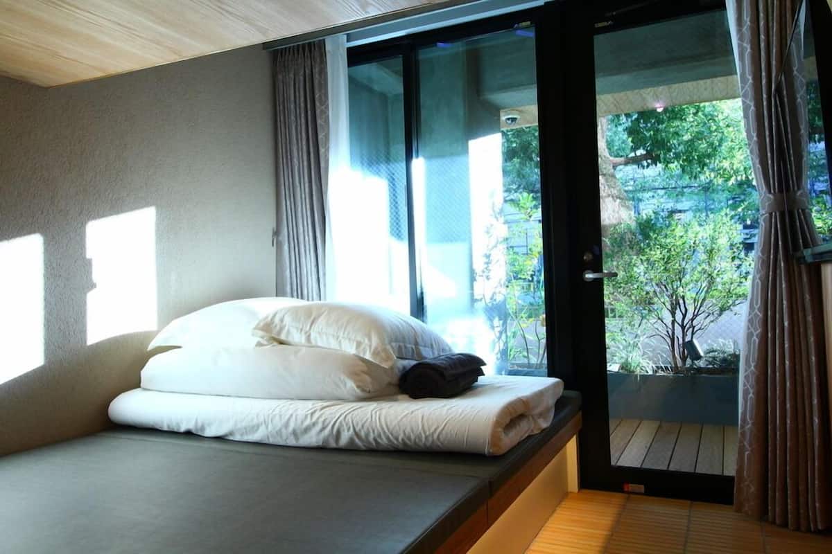 A bedroom with a bed, a sliding glass door, and a view of greenery outside.