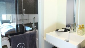 A modern bathroom with a glass shower enclosure, a white sink, and a large mirror. - Sakura Cross Hotel Tokyo Kayabacho (Tokyo)