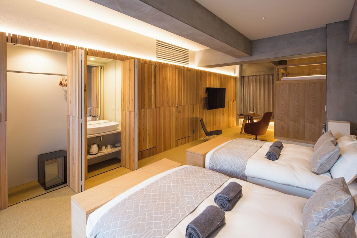 A hotel room with two beds, a sitting area, a TV, and a bathroom with a mirror and sink.