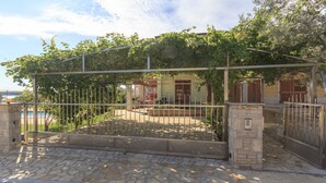 Un patio empedrado con una verja metálica, un muro de piedra y un edificio con una puerta y contraventanas rojas.