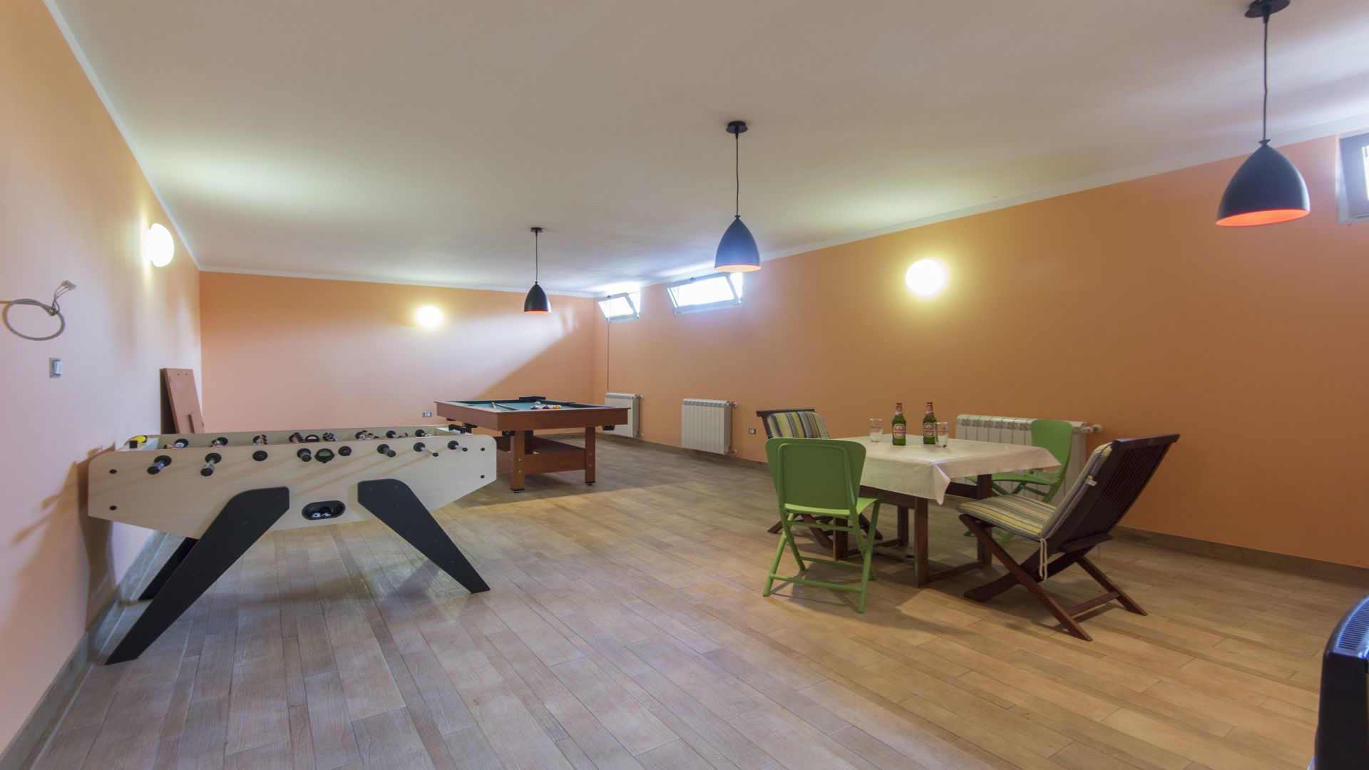 A room with a foosball table, pool table, and a dining area with chairs and a table.