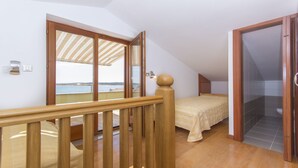 Un dormitorio con balcón, suelo de madera, una cama y vista al mar.