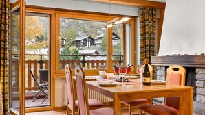 A dining area with a wooden table, red upholstered chairs, and a view of houses through large windows. - Silence by Interhome (Zermatt)