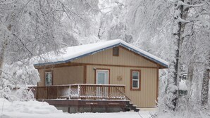 A wooden cabin with a porch and steps, surrounded by snow-covered trees.