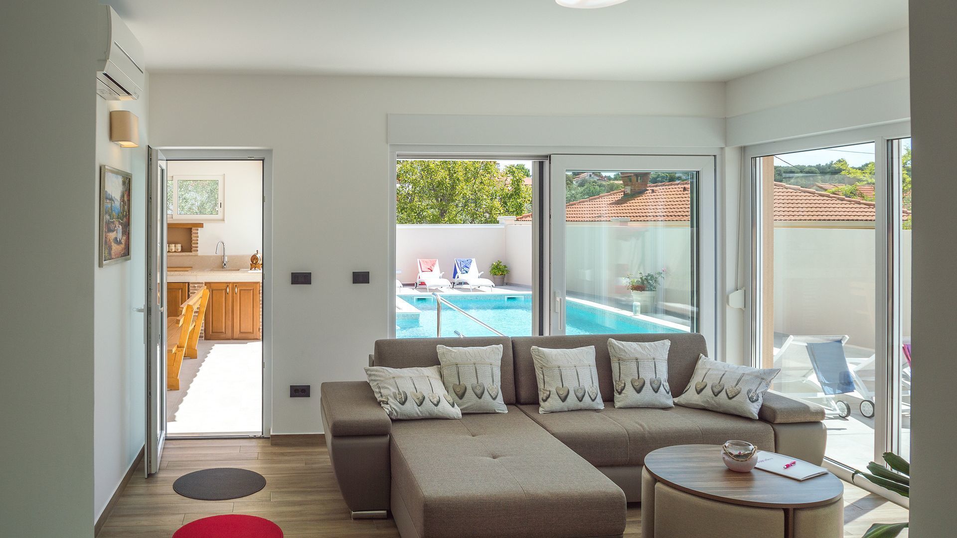 Ein modernes Wohnzimmer mit Sofa, Couchtisch und Blick auf ein Schwimmbecken sowie eine Sitzgruppe im Freien.