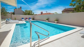 A rectangular swimming pool with a metal ladder, surrounded by lounge chairs and potted plants. - Villa Grannys House (Medulin)