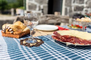 A table with a checkered tablecloth, a glass of water, a plate of sliced meats, a basket of bread, and a glass of wine. - Ethno House Kosic (Mokrine)