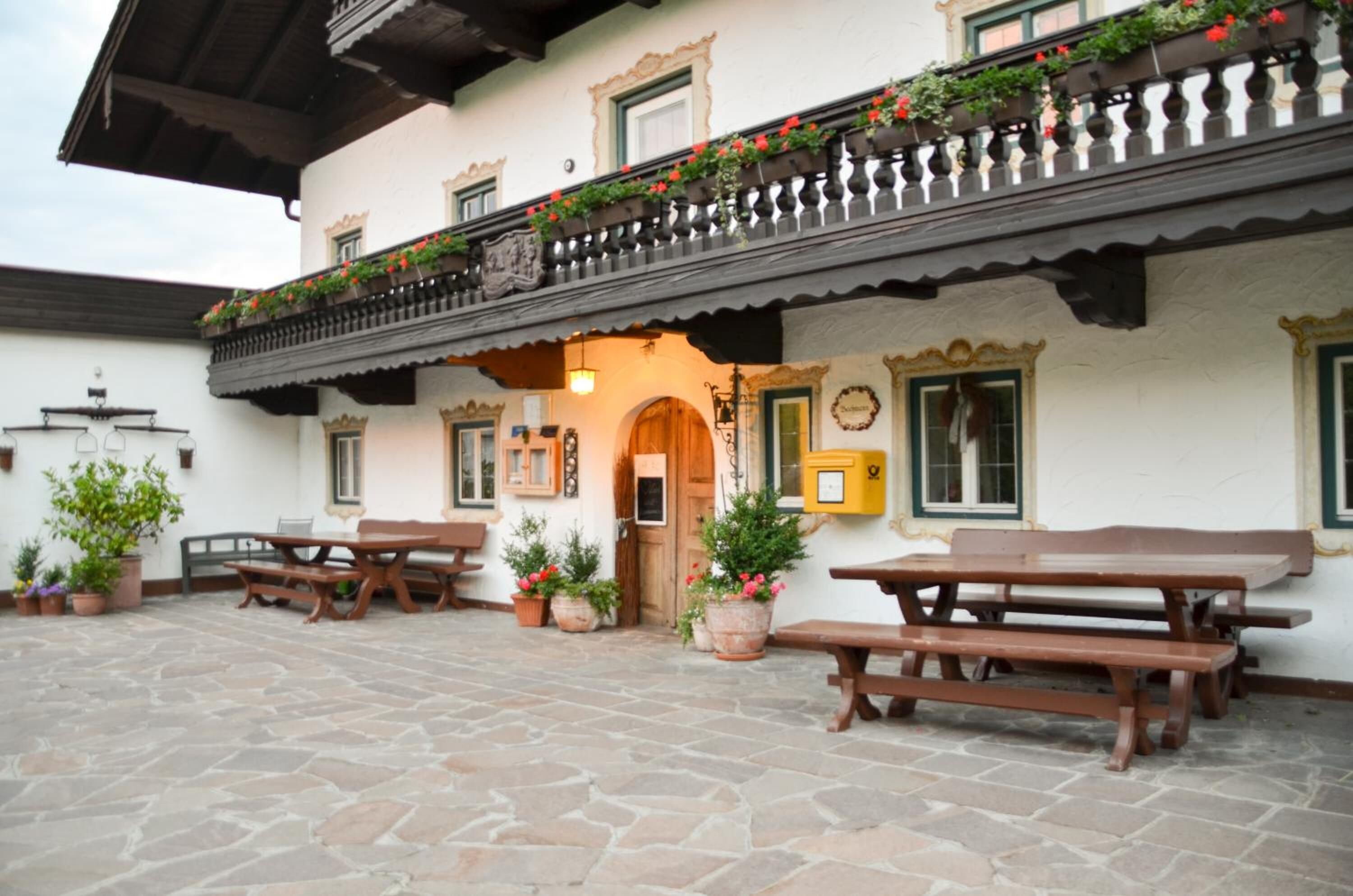 Ein traditionelles Gebäude mit einem pflastergelegten Innenhof, Holzbanken und Blumentöpfen.