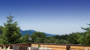 A terrace with outdoor seating, a view of mountains, and a clear sky. - Hotel Restaurant Alpenhof (Uebersee)