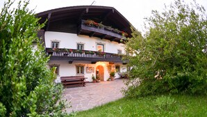 A traditional chalet with a stone-paved courtyard, wooden benches, and flower boxes on the balcony. - Hotel Restaurant Alpenhof (Uebersee)