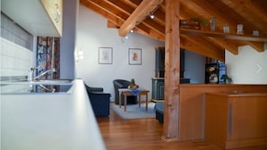 A modern kitchen with wooden beams, a dining area with a table and chairs, and a kitchen counter. - Hotel Restaurant Alpenhof (Uebersee)