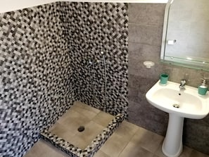 A bathroom with a checkered floor pattern, a shower, and a sink with a glass shelf above it. - Panorama View (Santorini)
