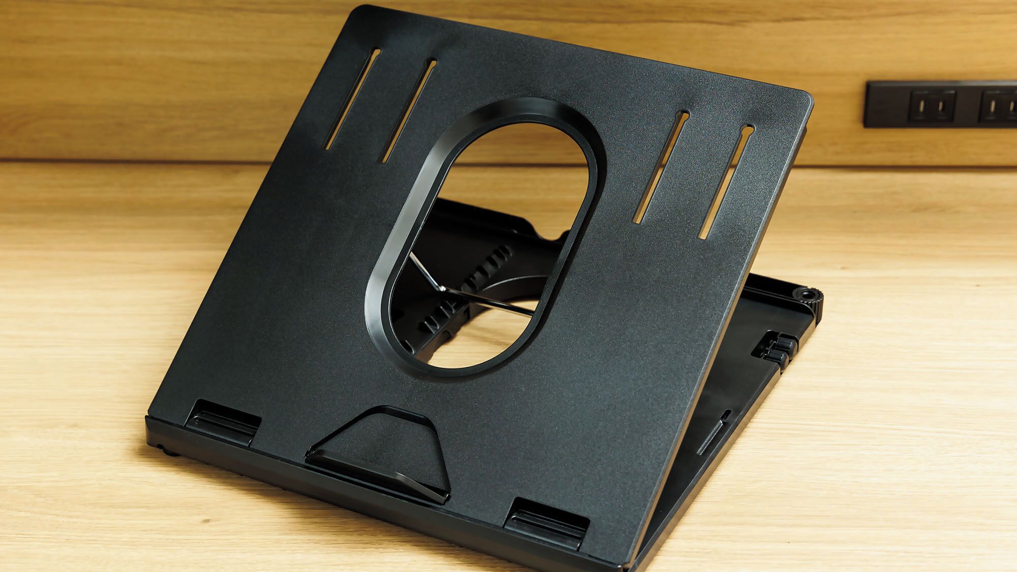Un oggetto nero a forma di quadrato con un foro centrale e fessure di ventilazione, posato su una superficie in legno.