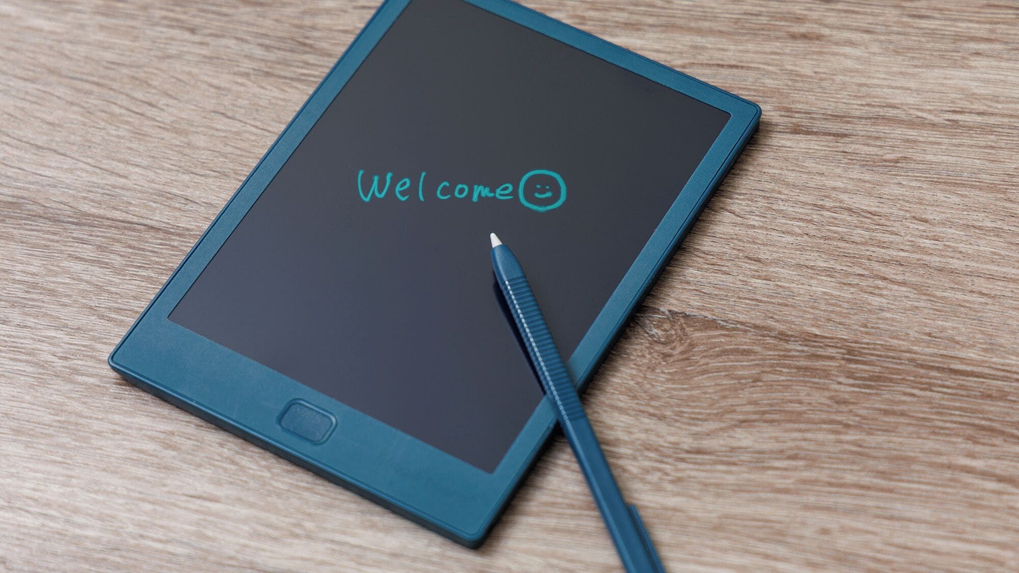 A tablet with "Welcome" and a smiley face on the screen, placed on a wooden surface.