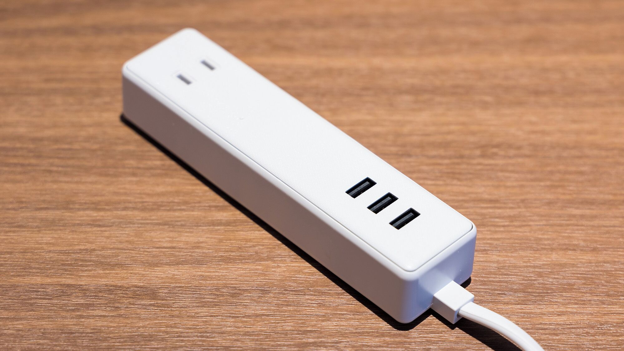 A white power strip with two USB ports and a standard electrical outlet on a wooden surface.