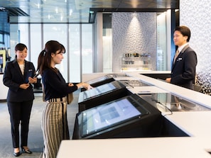A reception area with a modern design, featuring a reception desk, a digital information screen, and a decorative wall with a geometric pattern.