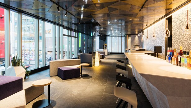 A modern bar area with a geometric ceiling design, seating arrangements, and a bar counter with various bottles. - JR East Hotel Mets Premier Akihabara (Tokyo)