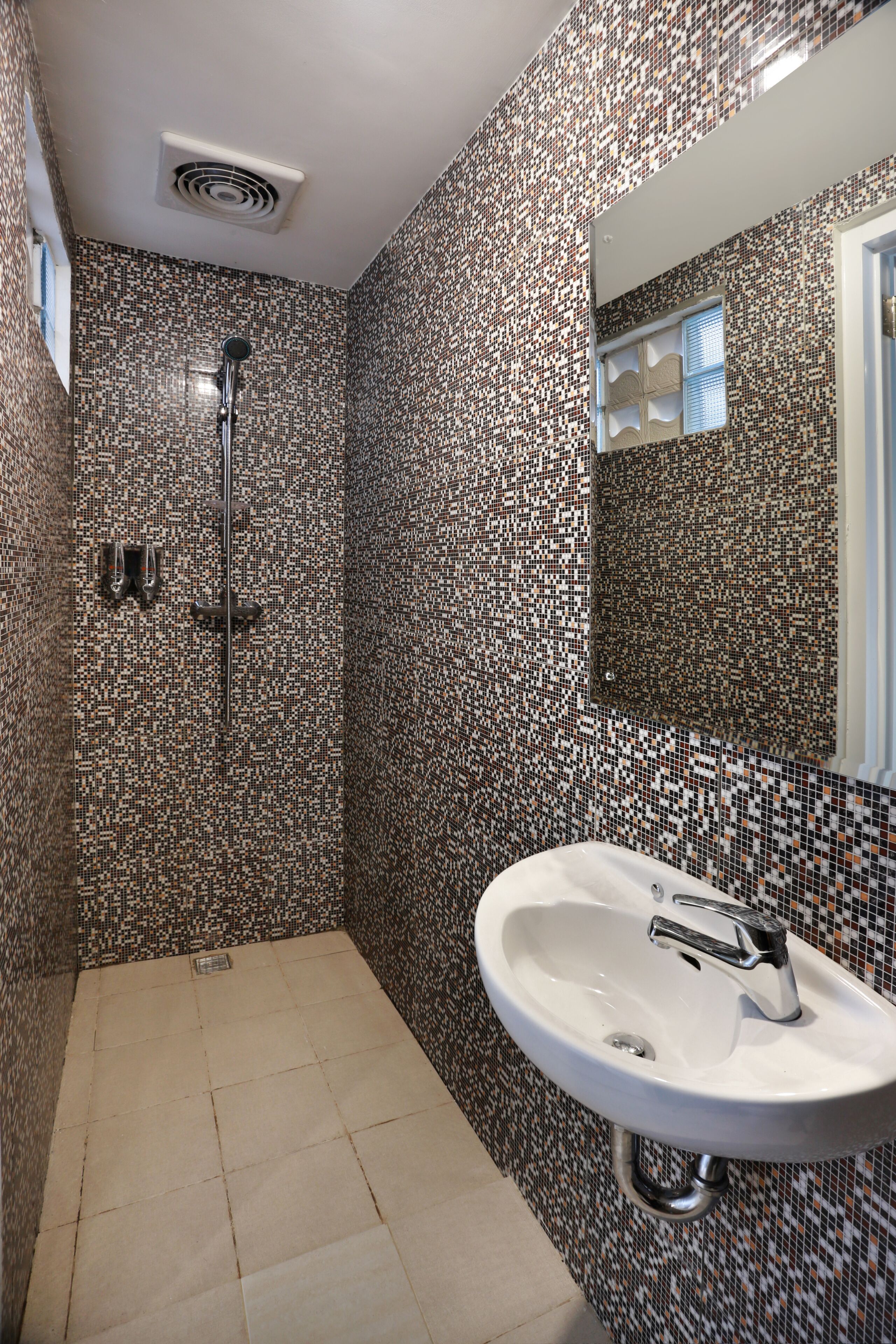 Un baño con ducha azulejada, lavabo y espejo.
