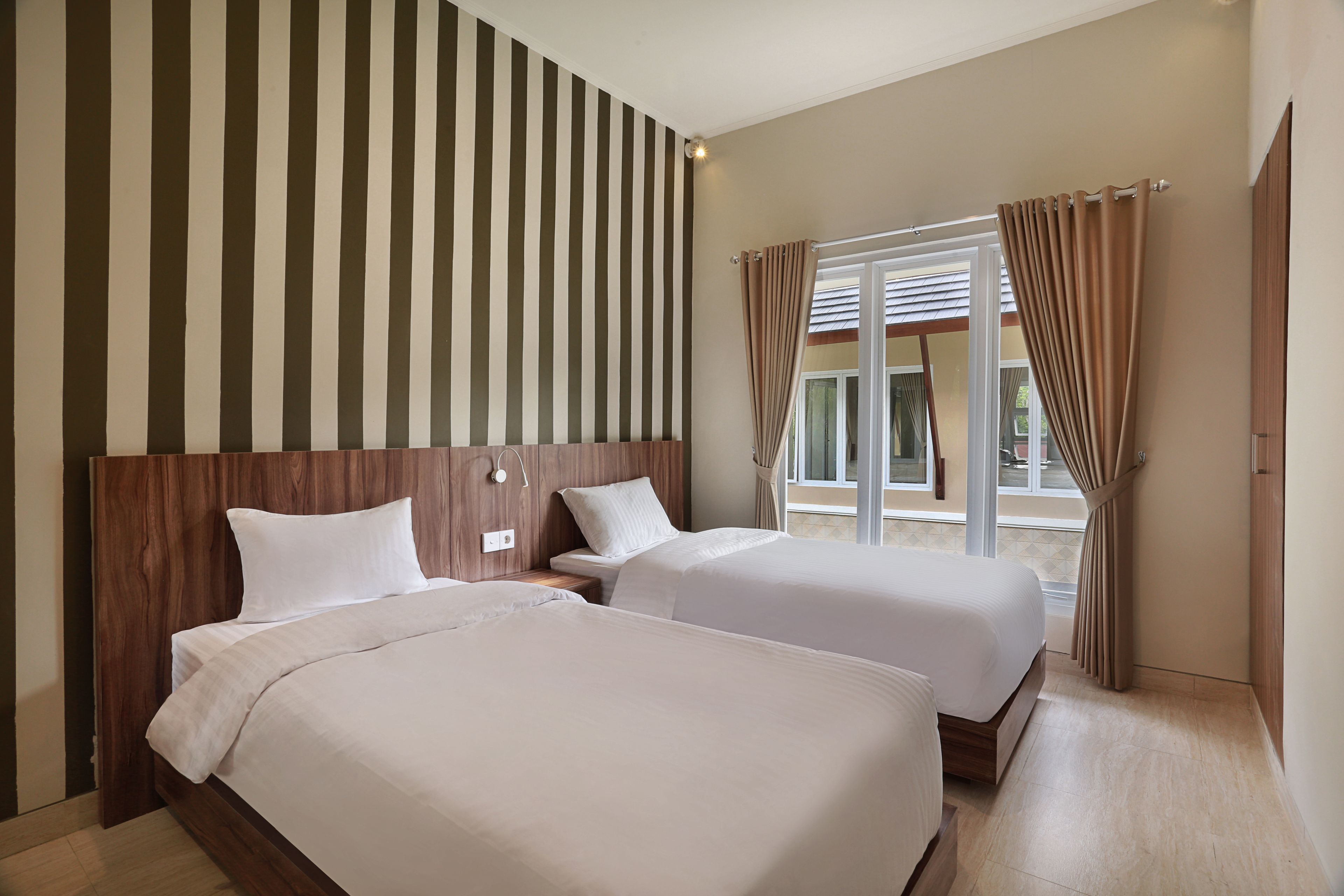 Quarto de hotel com duas camas, cabeceira de madeira, janela grande com cortinas e vista para o exterior.