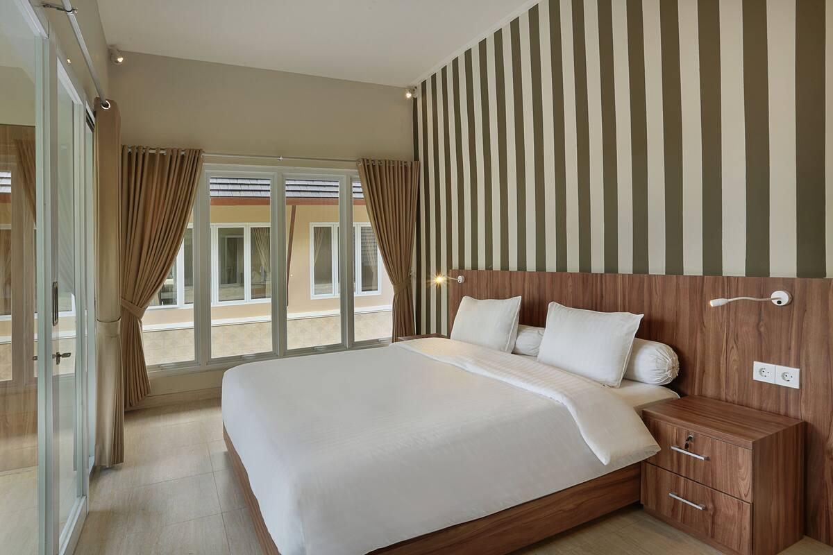 Een moderne hotelkamer met een groot bed, een houten hoofdeinde en uitzicht door de glazen deur.