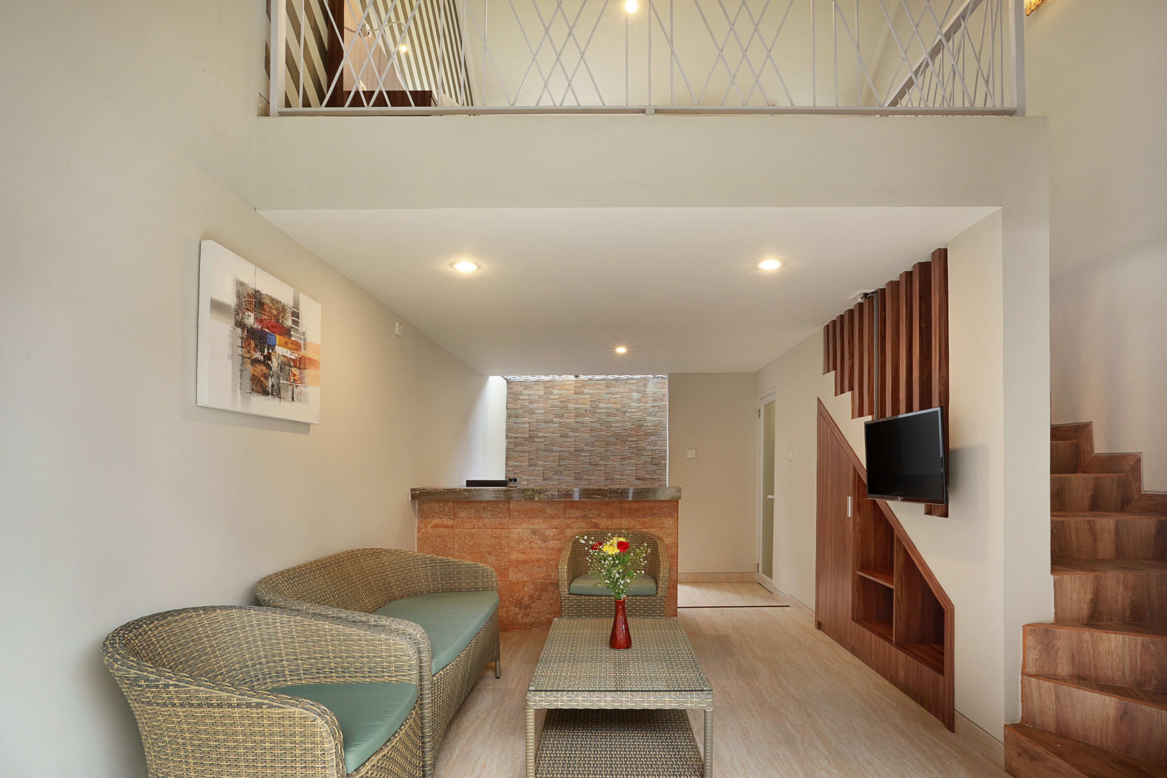 A living room with wicker furniture, a flat-screen TV, and a staircase.