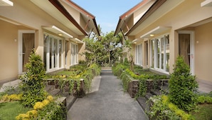 A corridor with a central pathway flanked by two buildings with large windows and a garden area with various plants.