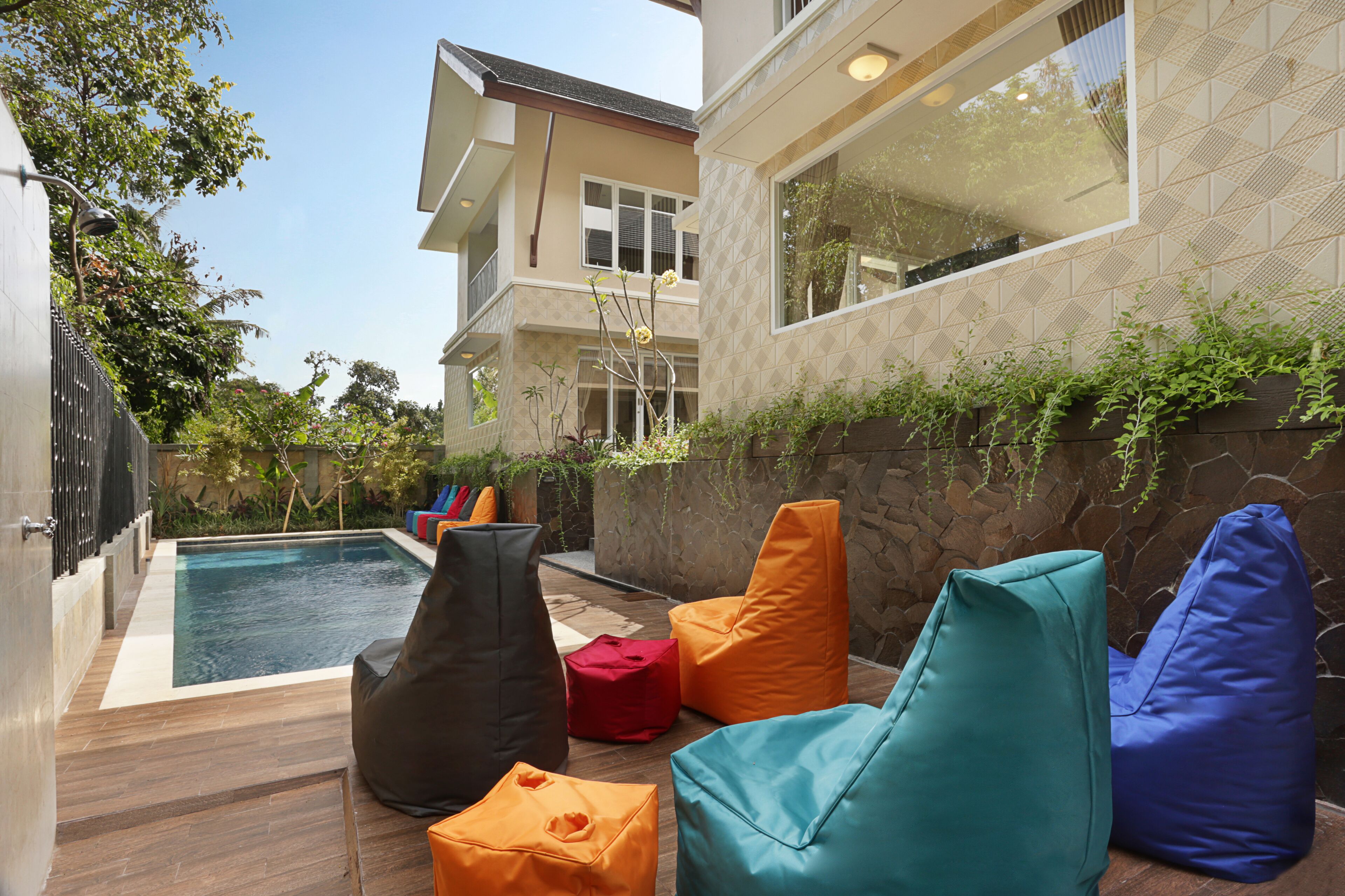 Zona de piscina con mobiliario moderno para exteriores y vista a un edificio de dos plantas.