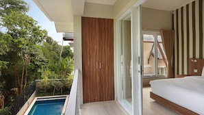 A bedroom with a large bed, a sliding glass door to a balcony, and a view of a swimming pool.