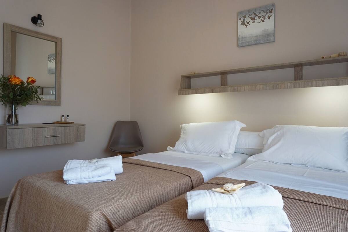 Habitación de hotel con una cama grande, una mesita de noche con artículos de aseo, una silla y un espejo.