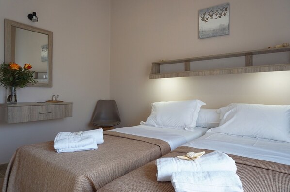 A hotel room with a large bed, a bedside table with toiletries, a chair, and a mirror. - Liprando (Paros)