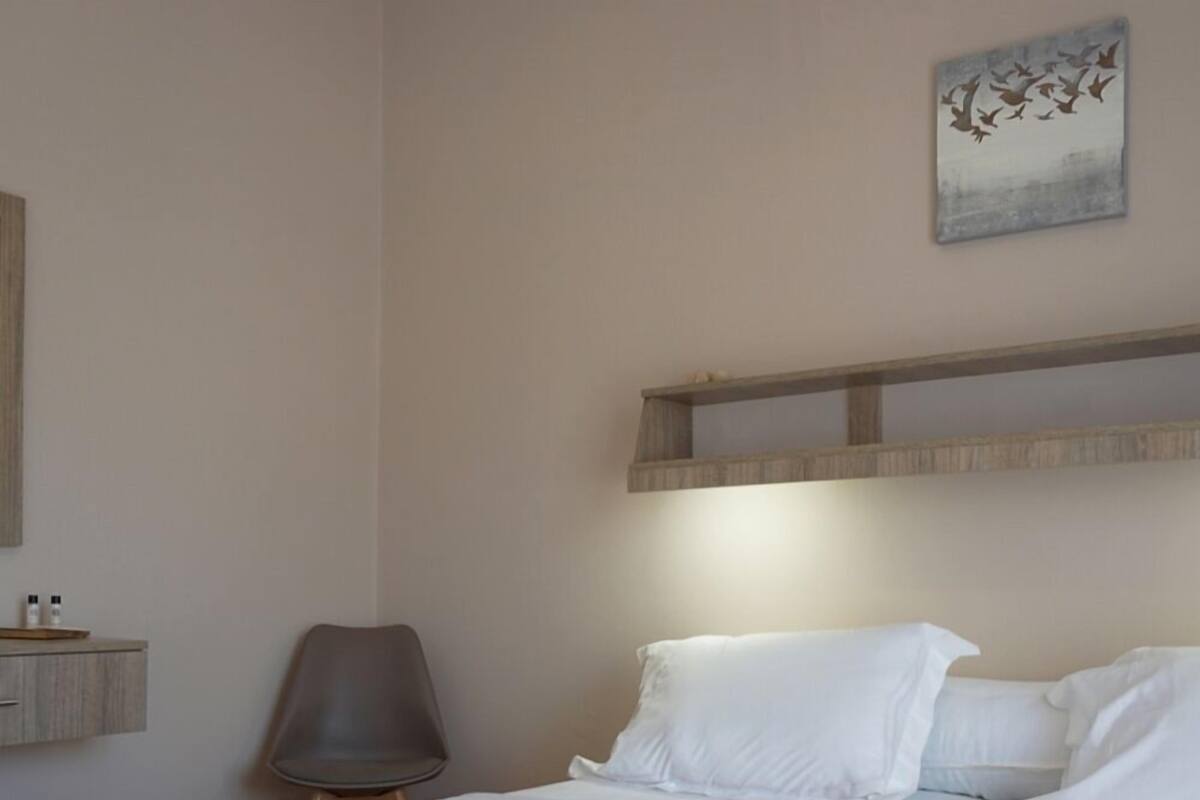 Habitación de hotel con dos camas, una silla, un estante con artículos de aseo y un cuadro en la pared.