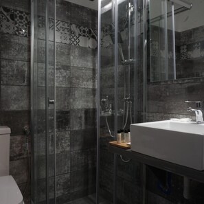 Une salle de bain dotée d’une douche à parois de verre, d’un lavabo blanc et d’un mur recouvert de carreaux formant un motif géométrique.